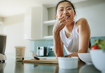 a person smiling and snacking while leaning on a kitchen counter