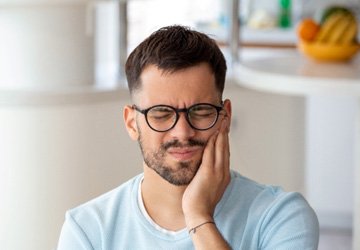 Man with glasses holding his cheek due to toothache