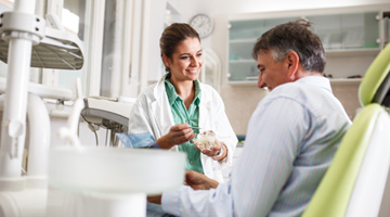 Smiling dentist showing patient model of teeth