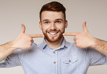 Young man with tooth-colored fillings smiling, pointing at teeth 