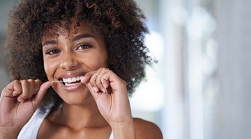 woman smiling while flossing her teeth 