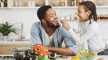 child giving their father a cherry tomato while cooking 