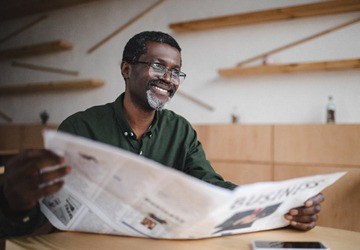 person smiling and reading the newspaper
