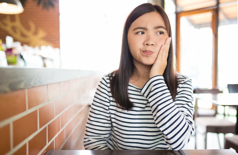 Woman in black and white striped blouse wincing and holding the side of her cheek in pain